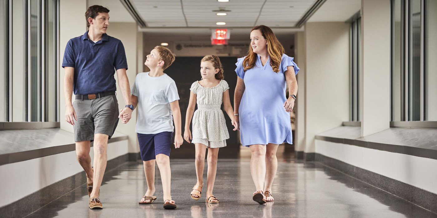 Joe, Emerson, Denver, and Stephanie McFadden walk down a hallway of the Duke Cancer Center. The McFadden Family walks down a hallway at Duke Cancer Center.
