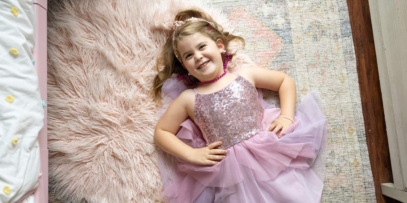 Dressed in her favorite color, Camden Fisher, age 6, poses for a photo in her room in Concord, NC. Camden Fisher, dressed in pink and sparkles, lays on the floor smiling up at the camera