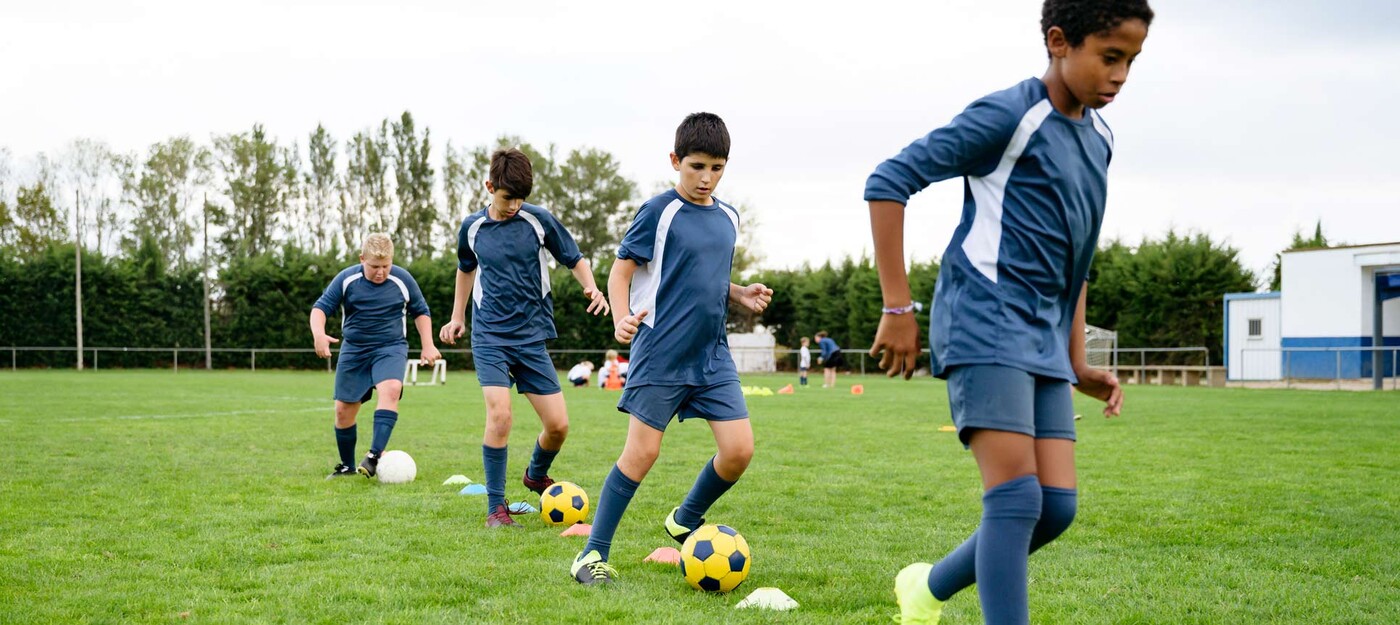 A youth boy's soccer team practices dribbling drills in a line around cones