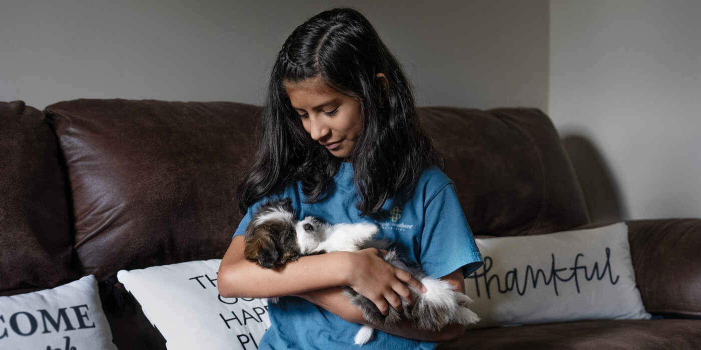 Giselle cuddles with the puppy she got after having heart surgery. The dog's name is Corazón, the Spanish word for "heart." Giselle sits on a couch holding her new puppy