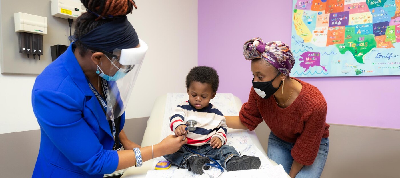 Gillian Noel, MD, shows her stethoscope to liver transplant patient, Noah Mann, as his mother, Talisha Becton (right), looks on. A provider shows a stethoscope to a young patient and his mother