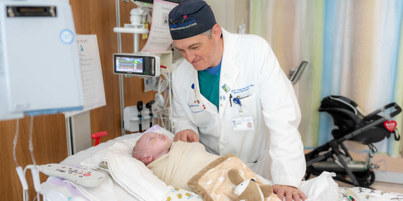 Duke pediatric heart surgeon, Joseph Turek, MD, PhD, visits with a patient recovering from a Norwood procedure. A doctor smiles at a baby in a hospital bed