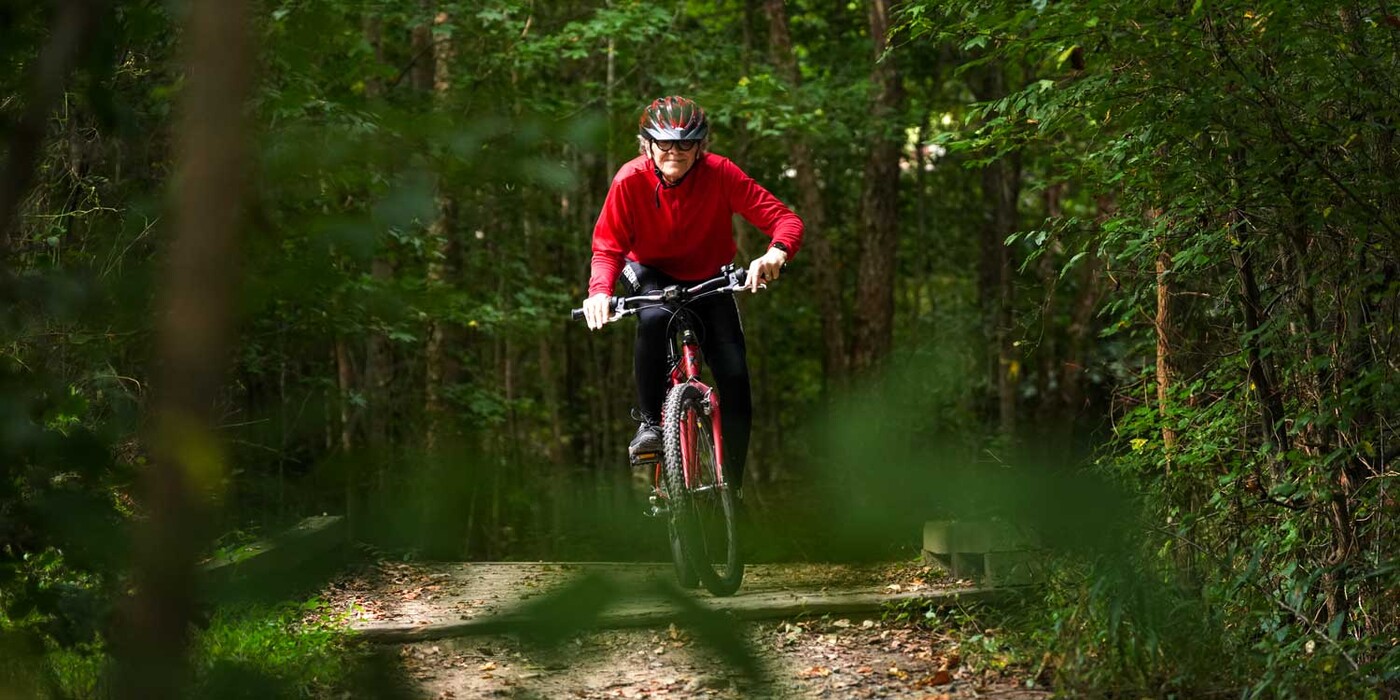 Steve Harlin enjoys maintaining his health by riding his bike on the trails near his Chapel Hill, NC home. Steve Harlin rides his bike across a wooden bridge on a forested trail.