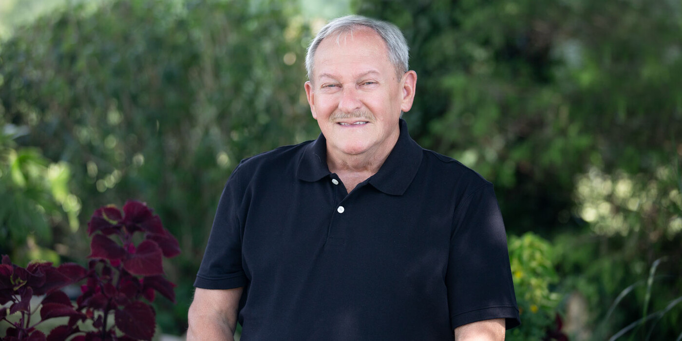 Dale Jessup, 71, smiles outside his home in Pinnacle, NC. Dale Jessup smiles in front of some greenery.